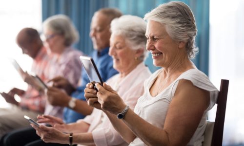 Row of smiling senior people sitting on chairs using digital tablets at retirement home
