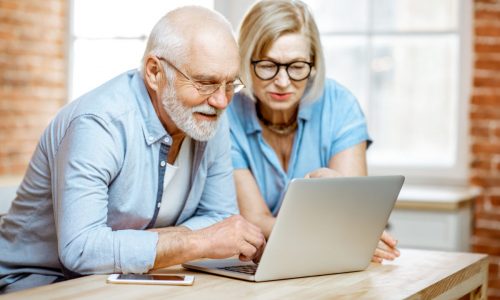 Portrait of a beautiful senior couple in blue shirts feeling happy, sitting together with laptop at home